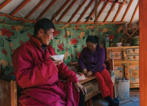 Mongolian man enjoying goat milk tea inside yurt with his family